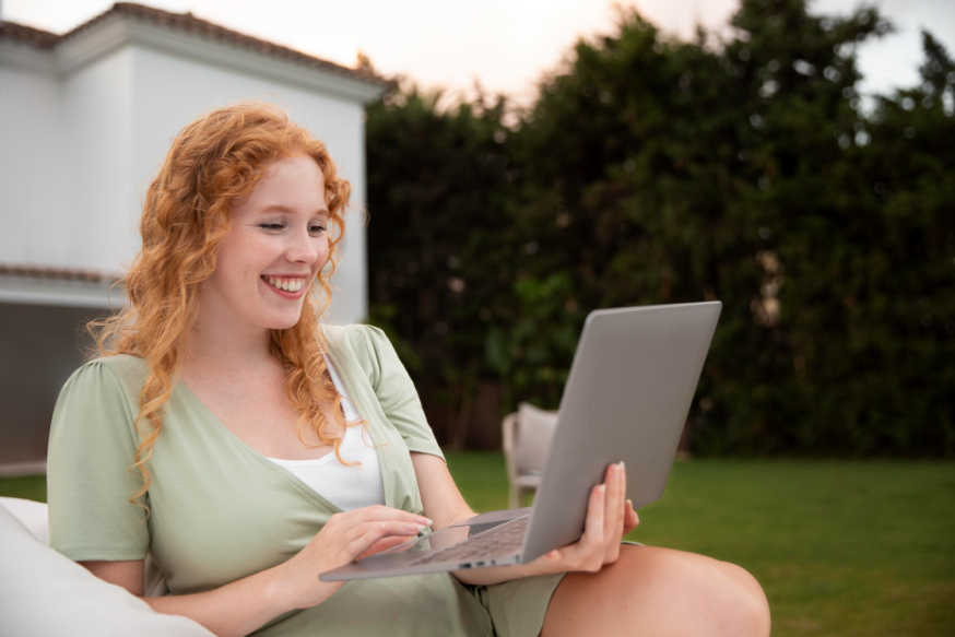 Image: Woman working happily with a laptop in a sunny, green garden by her home